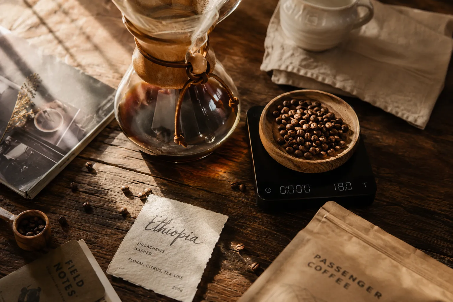 Editorial photography landscape (): overhead flat-lay of a rustic wooden café table with a Chemex glass coffee maker, a